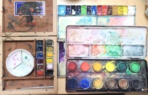 水彩画初心者が淡彩で風景画を描く際に、どんな絵の具を使うと良いかを紹介している画像。左はウィンザー&ニュートン社のパンカラー、右下はホルベインのケーキカラー、右上は小中学生が使用する安価な絵の具。いずれも固形化しているので水で溶かして使用する。