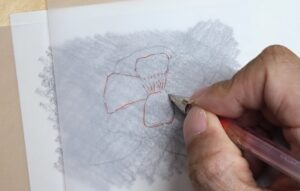 水彩紙、自作カーボン紙、下描きを清書したトレペの順に重ね、サザンカの下描きを赤ボールペンでなぞって転写している様子の画像。