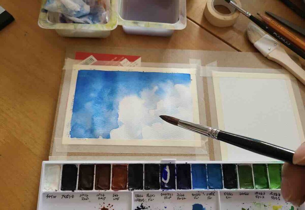 たっぷりの水を含ませた筆で、紙の上に鮮やかな青を広げている手元の写真