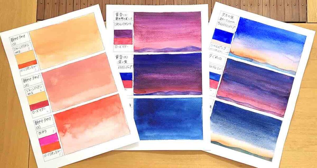 机の上に並べられた、朝焼けから夜空までの移ろいを描いた透明水彩のカラーチャート。