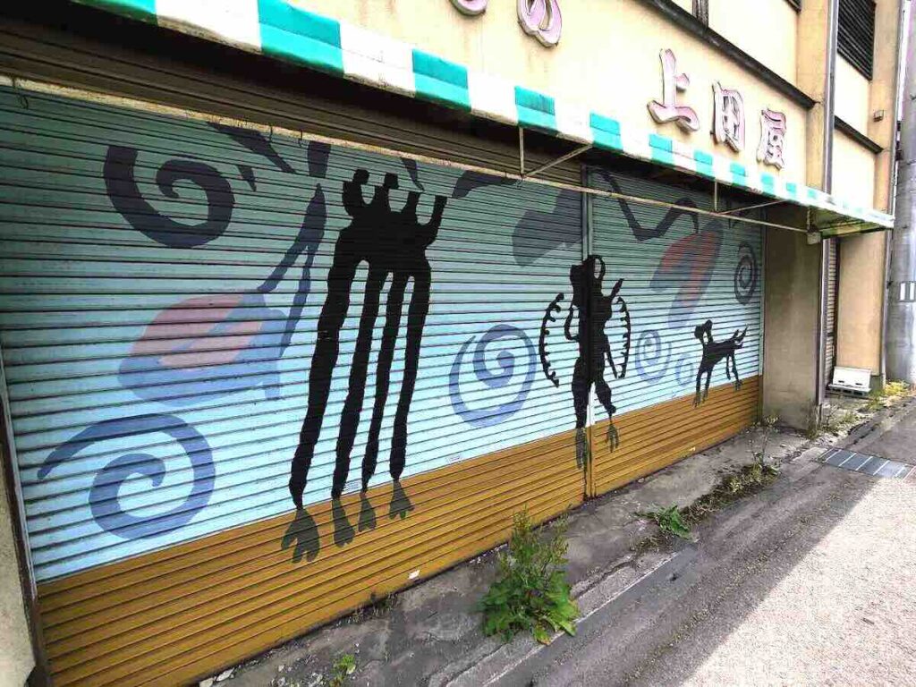 商店のシャッターに人物や動物のシルエットが描かれた壁画作品