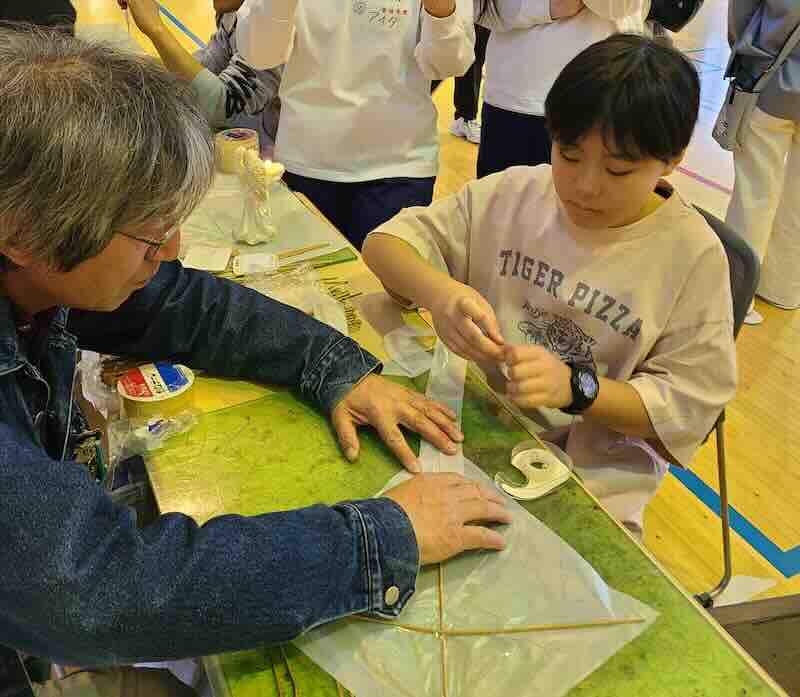 子どもが大人と一緒に凧作りを進めているワークショップ風景